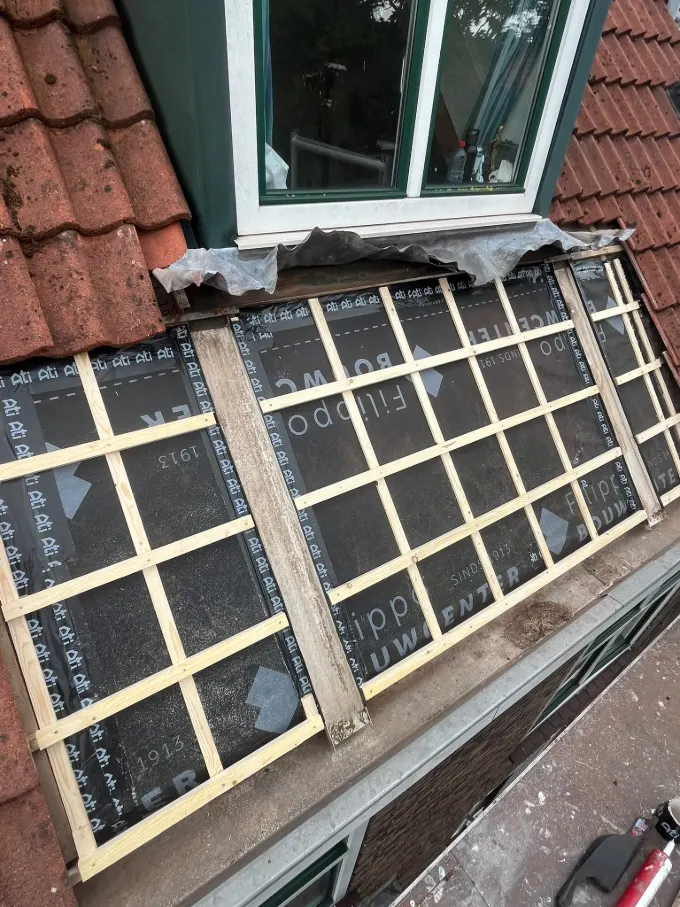 Nieuwe waterdichte folie en houten latten onder de dakpannen bij een dakkapel