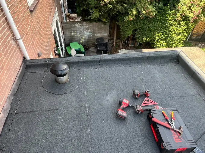 Nieuw bitumen plat dak met een ontluchtingspijp, naast een bakstenen gevel