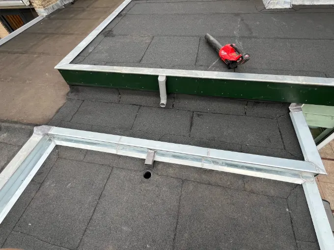 Nieuwe zinken dakranden en een zinken goot rond twee platte daken